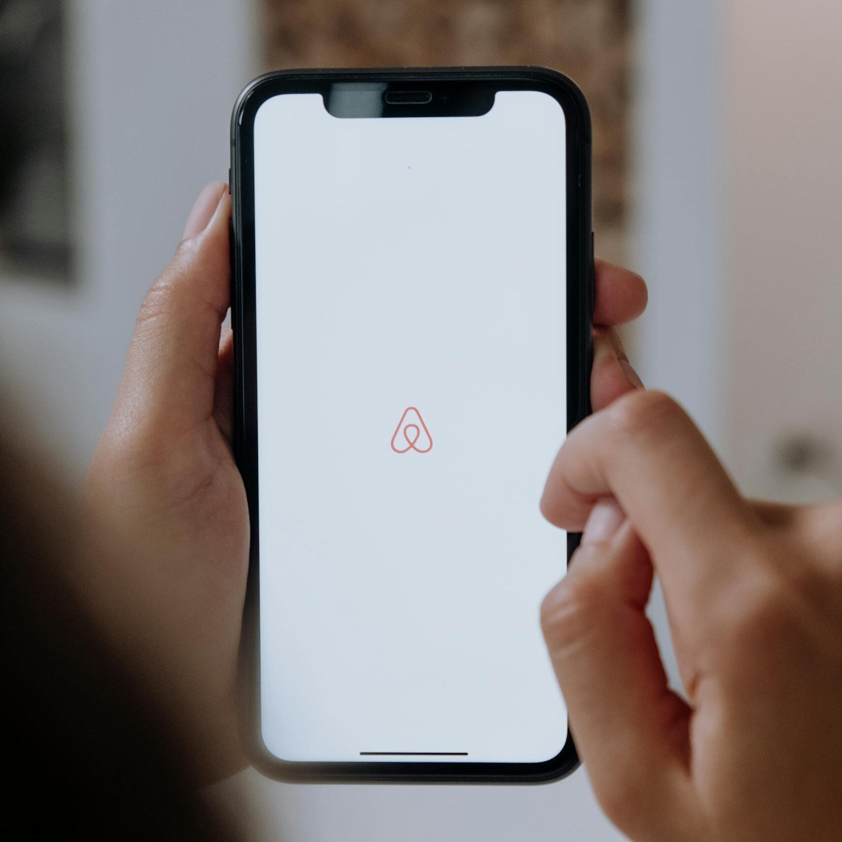 Close-up of hands holding a smartphone with Airbnb app logo on the screen indoors, highlighting modern technology.